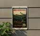 A vintage-style postage stamp depicting a mountain landscape with a small town in the foreground, mounted on a wall.