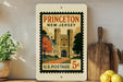 A vintage-style postage stamp from Princeton, New Jersey, featuring a castle and trees, displayed on a shelf next to a wooden cutting board and some lemons.