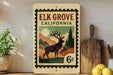 A vintage-style stamp depicting a deer in a forest setting, with the text "ELK GROVE CALIFORNIA" and a price of 6 cents.