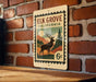 A metal sign with a vintage-style illustration of a deer standing in a forest, mounted on a brick wall.