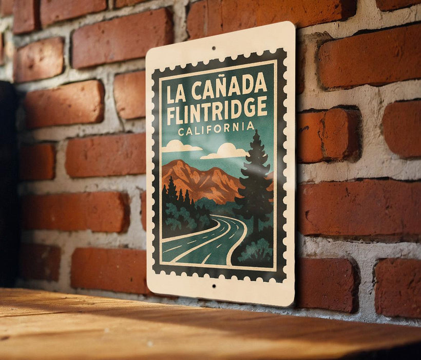 A metal sign with a vintage-style illustration of a road leading to a mountain range, mounted on a brick wall.
