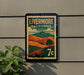 A vintage-style postage stamp from California, featuring a landscape with mountains, hills, and a tree, mounted on a wall.