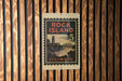 A vintage-style postage stamp from Illinois, featuring a scenic landscape with a bridge and a tower, is displayed on a wooden wall.