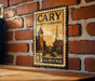 A vintage-style postage stamp from North Carolina, featuring a clock tower and other architectural elements, is displayed on a brick wall.