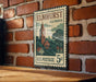 A vintage postage stamp from Illinois, featuring a brick wall and a clock tower, is displayed on a wooden surface.