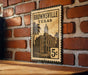 A vintage-style metal sign with the text "BROWNSVILLE TEXAS" and an illustration of a building, mounted on a brick wall.