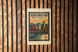 A wooden wall with a vintage-style postage stamp featuring an illustration of a cityscape and a bridge, mounted on it.