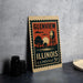 A vintage postage stamp from Illinois, featuring an illustration of a water tower and a sunset, is displayed on a table.