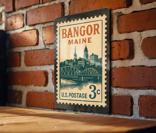 A vintage postage stamp from Bangor, Maine, featuring a cityscape and a bridge, is displayed on a brick wall.