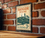 A vintage postage stamp from Bangor, Maine, featuring a cityscape and a bridge, is displayed on a brick wall.