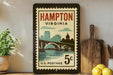 A vintage postage stamp from Hampton, Virginia, featuring a cityscape and a bridge, displayed on a shelf next to a wooden cutting board and some lemons.