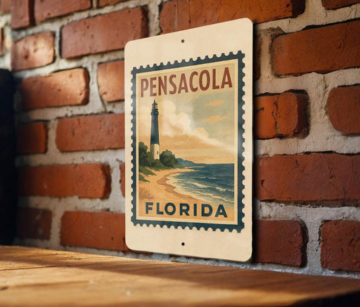 A vintage-style sign for Pensacola, Florida, featuring a lighthouse and beach scene, mounted on a brick wall.