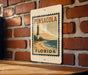 A vintage-style sign for Pensacola, Florida, featuring a lighthouse and beach scene, mounted on a brick wall.