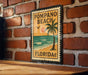 A vintage-style metal sign with the text "POMPAO BEACH FLORIDA" is displayed on a brick wall.