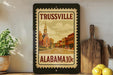A framed stamp depicting Trussville, Alabama, with a church steeple and a street scene.