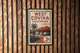 A vintage-style West Covina, California postage stamp is displayed on a wooden wall.