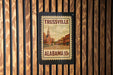 A framed poster of Trussville, Alabama, with a church and buildings depicted, is mounted on a wooden wall.