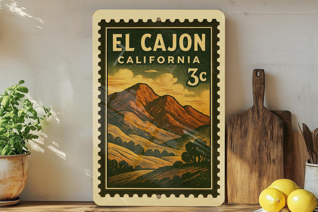 a vintage-style postage stamp from El Cajon, California, with a mountain landscape and a 3c denomination. The stamp is displayed on a shelf next to a wooden cutting board and a potted plant.