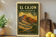 a vintage-style postage stamp from El Cajon, California, with a mountain landscape and a 3c denomination. The stamp is displayed on a shelf next to a wooden cutting board and a potted plant.