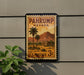 A vintage U.S. postage stamp from Nevada, featuring a desert landscape with palm trees and mountains, mounted on a wall.