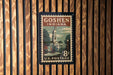 A vintage postage stamp from the United States, featuring an illustration of a building and a clock, mounted on a wooden wall.