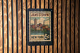 A vintage-style postage stamp from New York, featuring a cityscape and a clock tower, is displayed on a wooden wall.