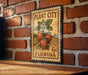 A vintage-style metal sign with a strawberry illustration and text, mounted on a brick wall.