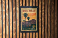 A vintage-style postage stamp from California, featuring a palm tree and sunset landscape, is displayed on a wooden wall.