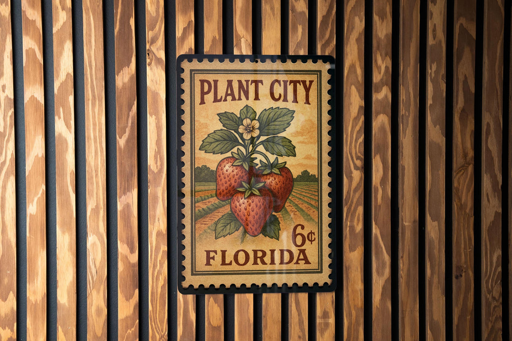 A vintage-style stamp or label with a strawberry plant and the text "PLANT CITY FLORIDA" printed on it, mounted on a wooden wall.
