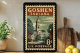 A vintage postage stamp from Goshen, Indiana, displayed on a shelf next to a wooden cutting board and some potted plants.