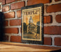 A metal sign with a vintage-style illustration of a building, mounted on a brick wall.