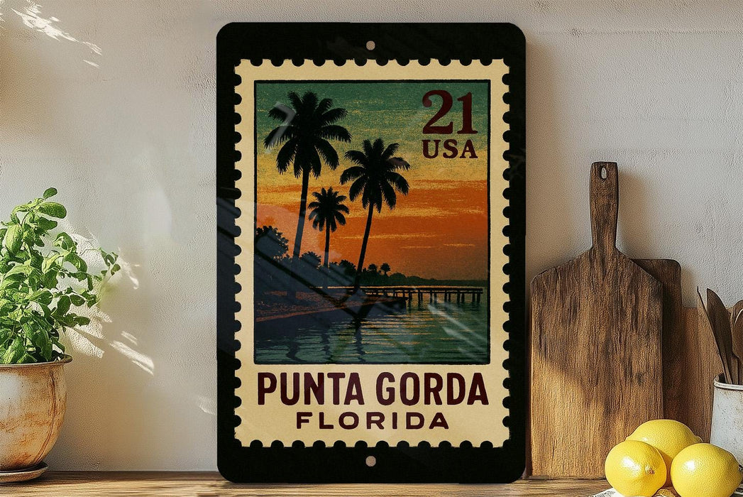 A framed vintage postage stamp depicting a tropical beach scene with palm trees and a sunset, placed on a shelf next to a wooden cutting board and a potted plant.
