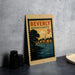A vintage postage stamp from Beverly, Massachusetts, featuring a scenic landscape with a river and houses, is displayed on a countertop.