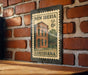 A metal sign with a brick wall in the background, featuring a vintage-style illustration of a building and the text "NEW IBERIA U.S. 6¢ LOUISIANA".