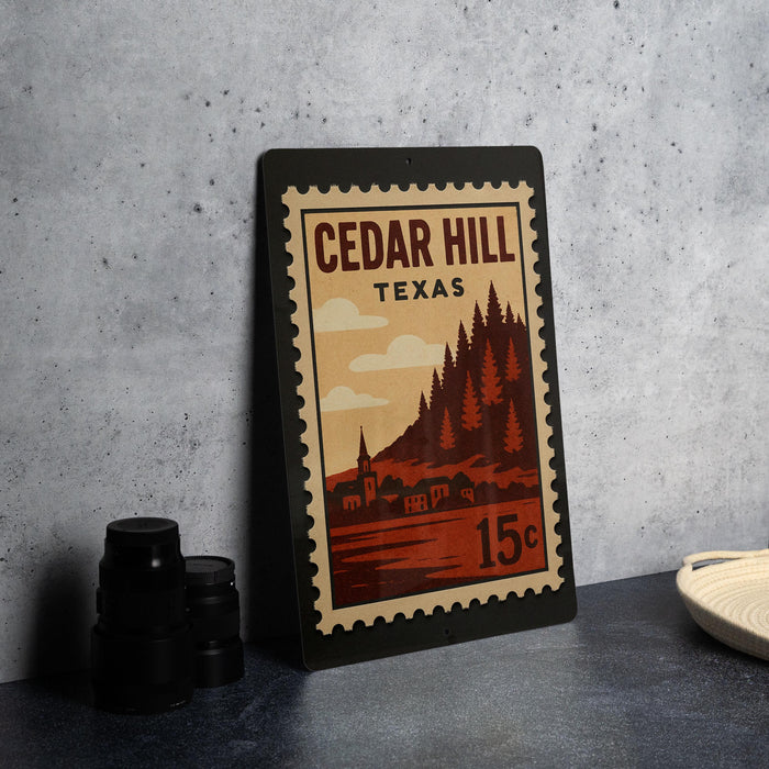 A vintage-style postage stamp from Cedar Hill, Texas, featuring a landscape with a town and pine trees, placed on a countertop next to some black camera lenses.