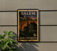 A framed vintage postage stamp from Salem, Massachusetts, featuring a house and a church, is displayed on a wall next to a plant.