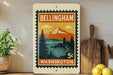 A vintage-style postage stamp from Washington, featuring a mountain landscape with a castle, is displayed on a shelf next to a wooden cutting board and some potted plants.