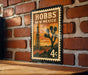 A vintage-style postage stamp from New Mexico featuring a desert landscape with a tall tower in the background.