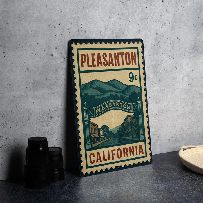 A metal stamp with a vintage design, featuring a street scene and mountains, is displayed on a table next to some black camera lenses.