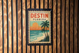 A vintage-style stamp or sign with the text "DESIN FLORIDA" displayed prominently, featuring a tropical beach scene with palm trees and a sunset.