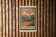 A metal sign with a vintage-style illustration of a town and countryside, mounted on a wooden wall.