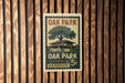 A vintage-style postage stamp from Oak Park, Illinois, featuring a tree and a building, is displayed on a wooden wall.
