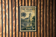 A vintage postage stamp from the United States of America, featuring a building and palm trees, mounted on a wooden wall.