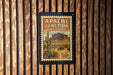 A vintage postage stamp from Arizona, featuring a desert landscape with mountains and cacti, is displayed on a wooden wall.