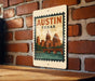 A metal sign with a vintage-style illustration of Austin, Texas, mounted on a brick wall.