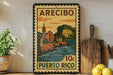 A vintage-style poster of Puerto Rico, featuring a coastal town scene with a church and mountains in the background, is displayed on a wall next to a wooden cutting board and a potted plant.