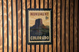 A vintage-style postage stamp depicting the Monument to the Colorado River, with the text "MONUMENT 8c COLORADO" printed on it.