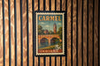 A vintage postage stamp from Indiana featuring a bridge and a clock tower, mounted on a wooden wall.