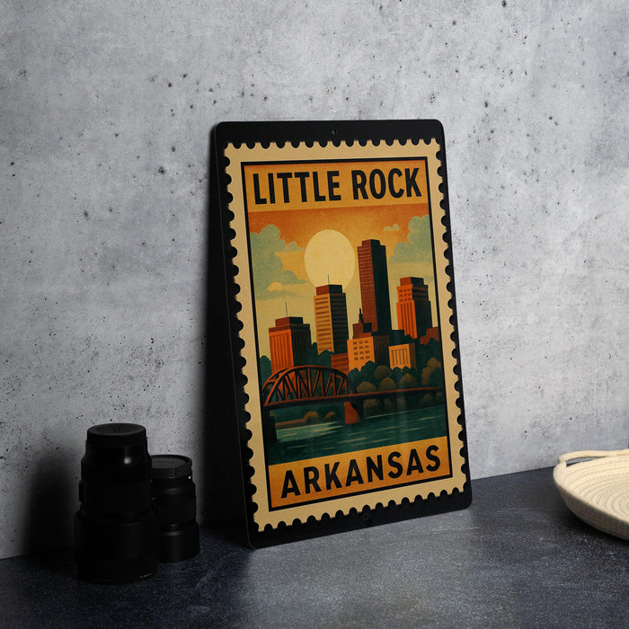 A framed poster of Little Rock, Arkansas, featuring a cityscape with a bridge and a sunset in the background.