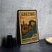 A vintage Puerto Rico postage stamp featuring a coastal town scene, placed on a countertop next to some black camera lenses.